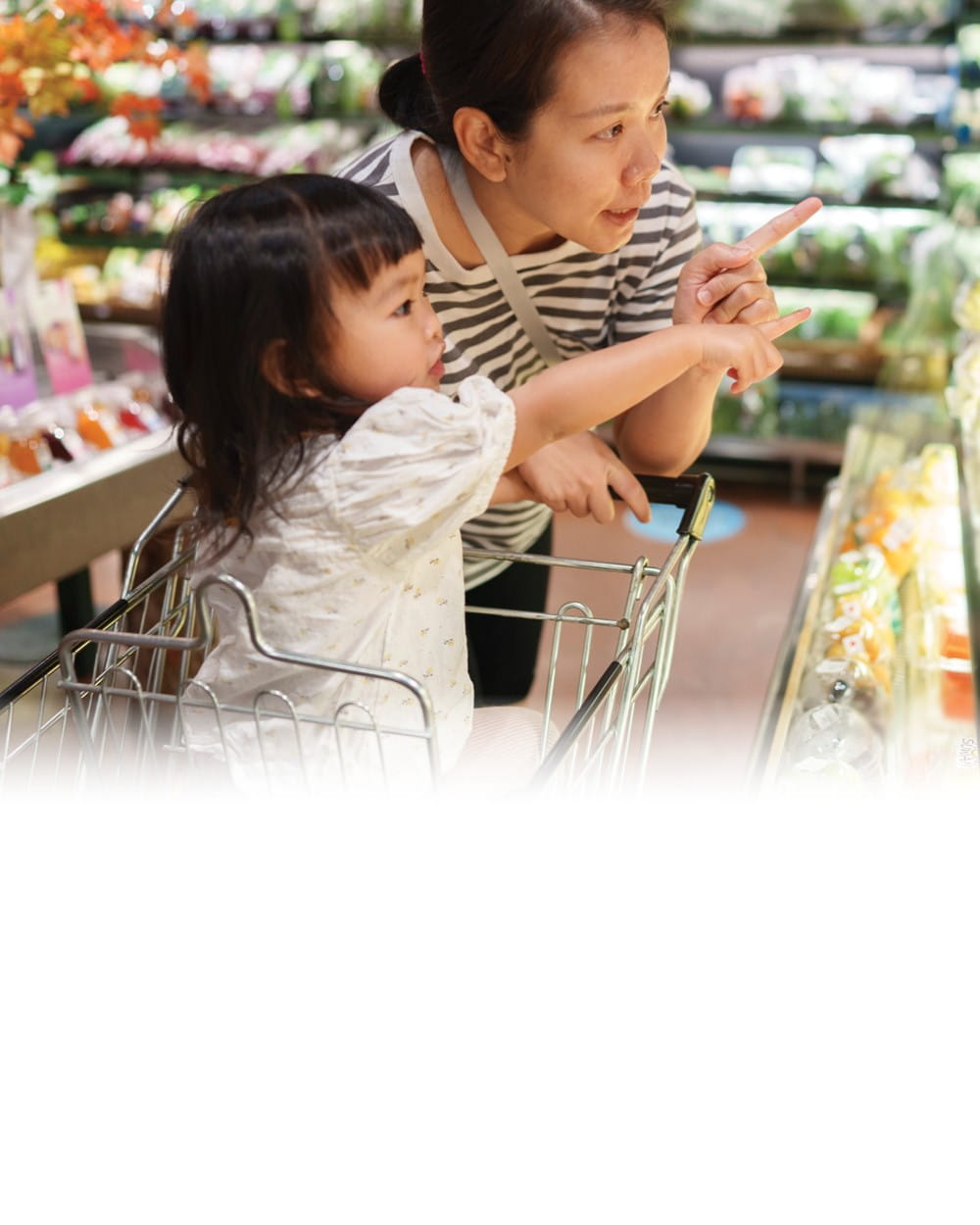 A mother and child point toward produce at a grocery store.