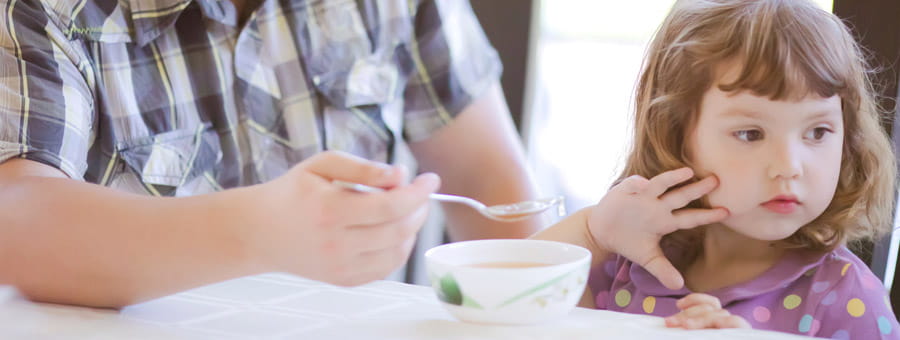 Person in a plaid shirt holds a spoon in front of a young child
