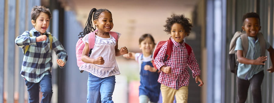 Group of happy children running down school walkway.