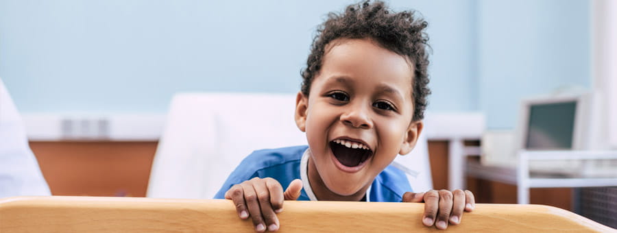 Smiling boy patient with curly hair in hospital bed.