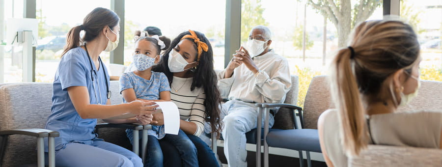 Nurse speaks with masked parent and child in emergency department waiting room.