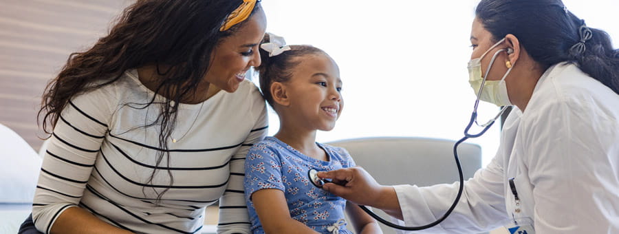 Mother sits with her daughter while she is examined by doctor.