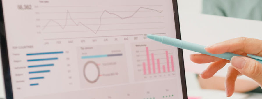 A hand holding a pen points at a series of graphs on a screen