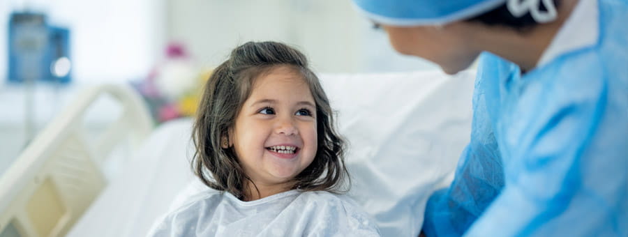 Young girl in hospital bed speaks to doctor.