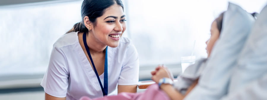 Nurse talking with child patient in hospital bed.