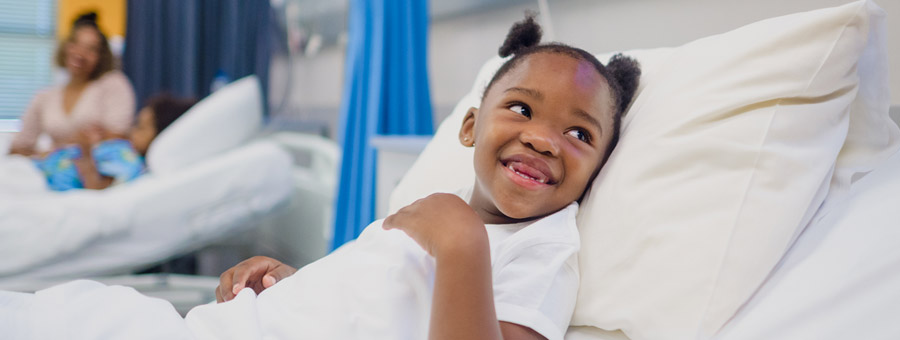 Smiling child laying in a hospital bed.