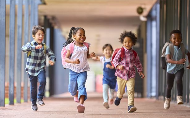 Group of happy children running down school walkway.