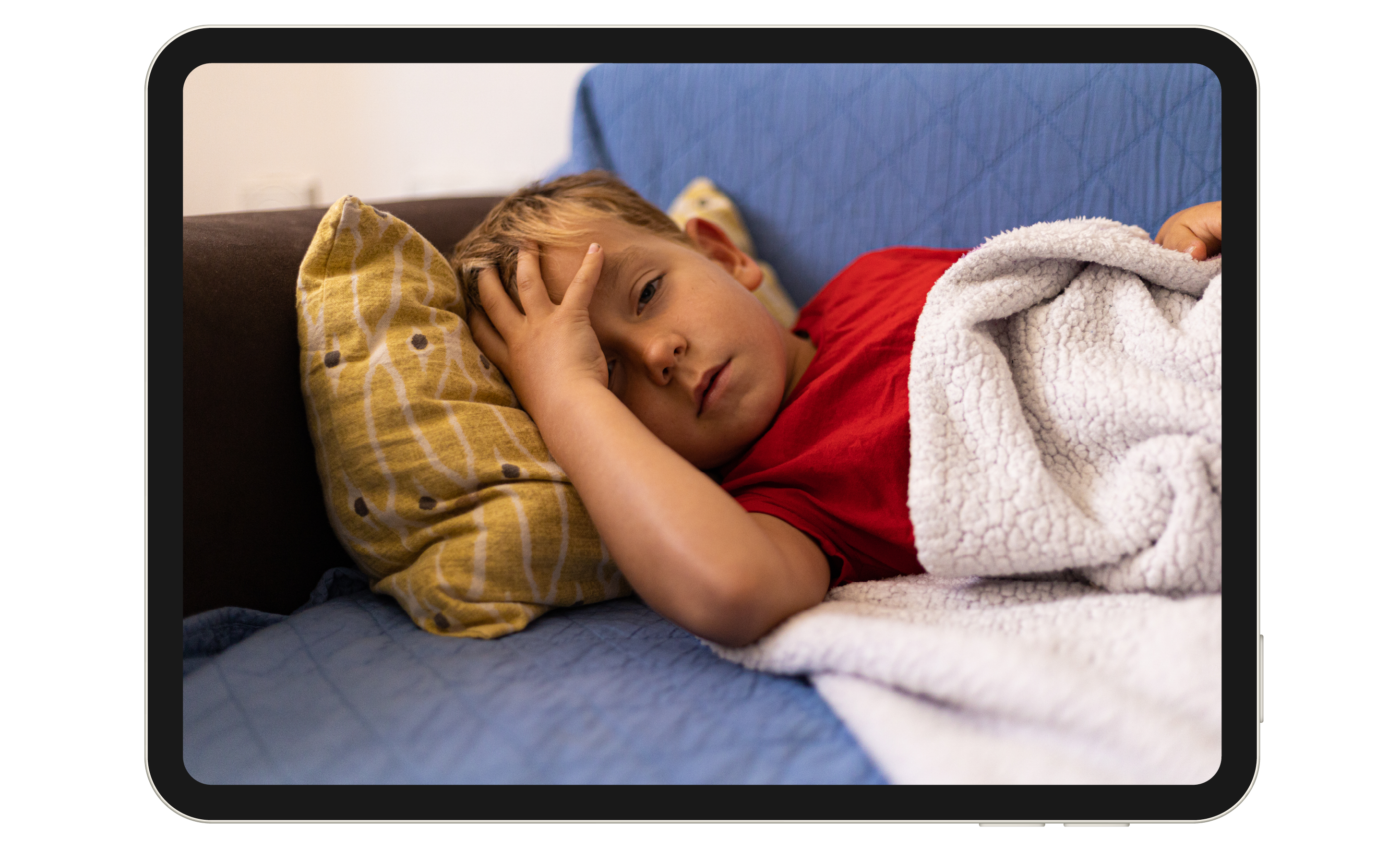 A young child rests on a couch, holding their head.