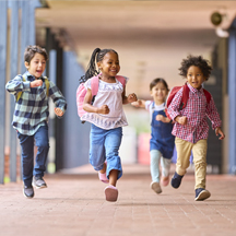 Group of happy children running down school walkway.