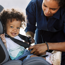 Toddler being strapped into a car seat.