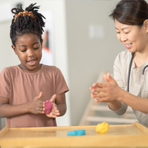 Young girl and her therapist work with modeling clay together.