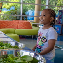 Child smiling in front of salad being prepped