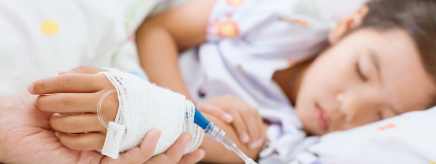Child in hospital bed, caregiver holding hand.